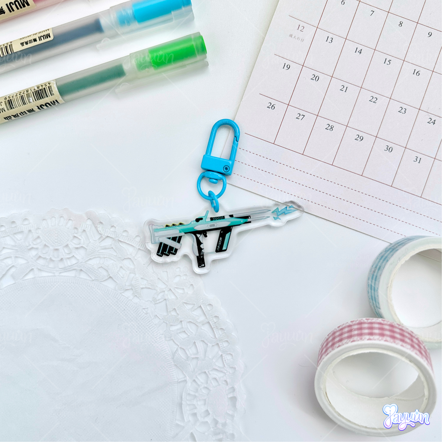 Teal Arc-inspired rifle acrylic charm photographed on a white desk background.