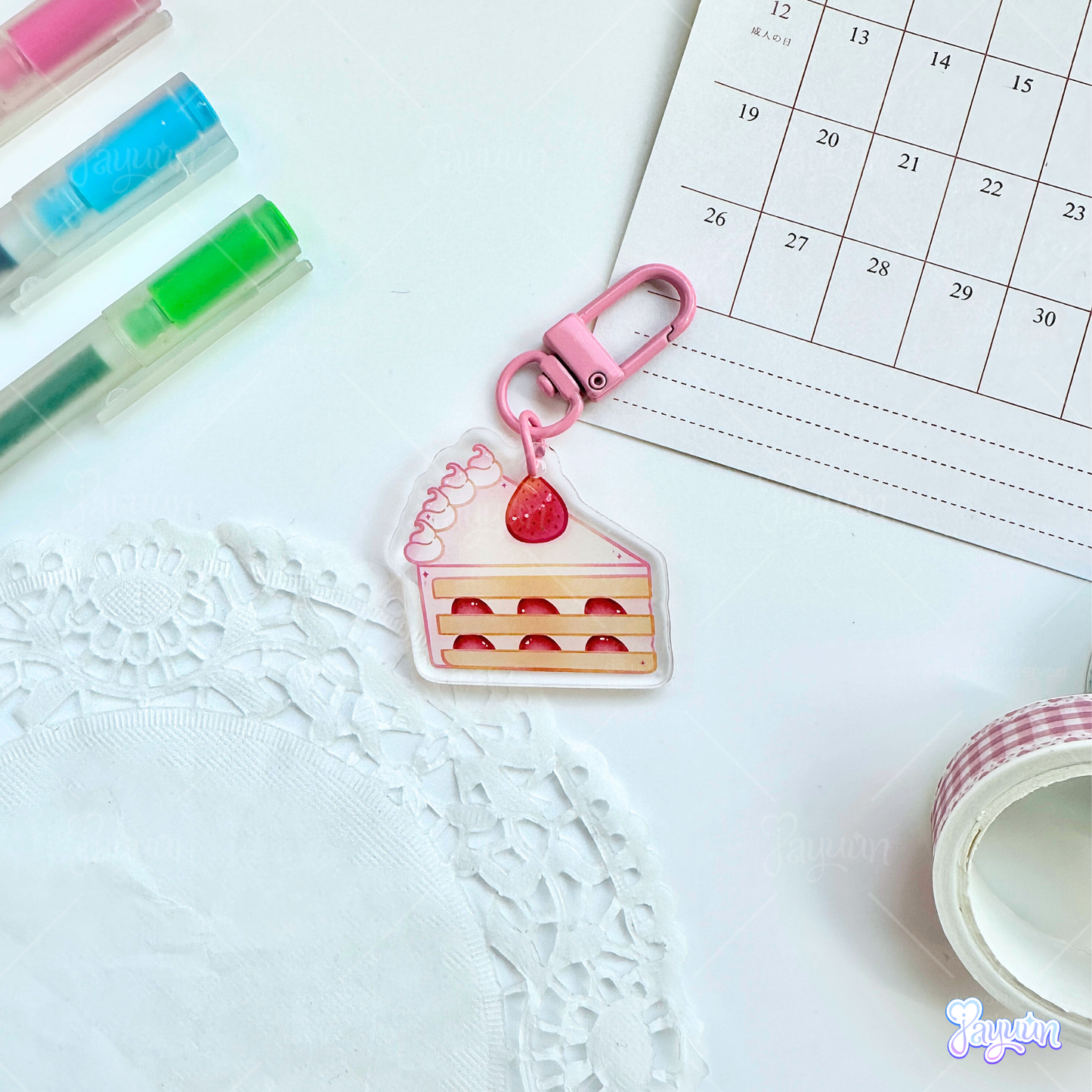 Strawberry cake slice acrylic keychain photographed on a white desk background.