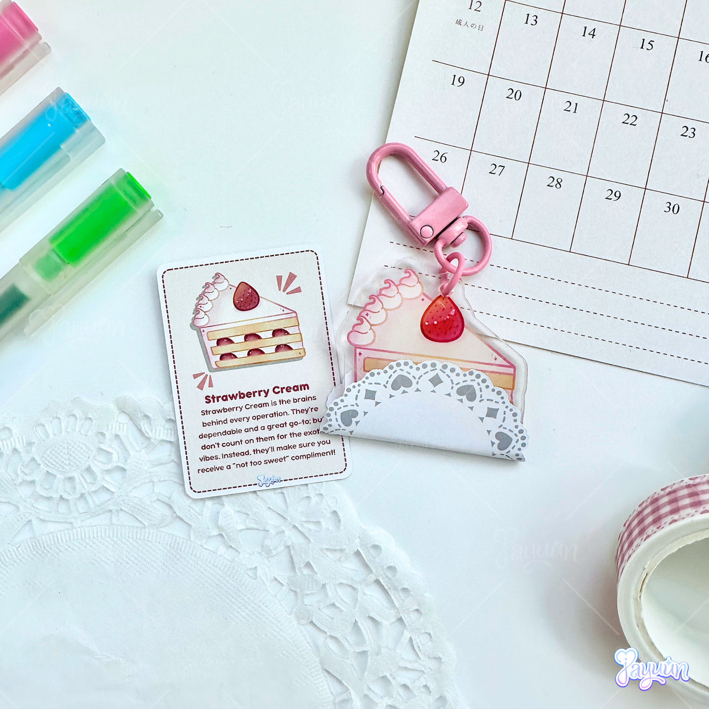Strawberry cake slice acrylic keychain wrapped in a mini doily, photographed alongside a mini collectible card.