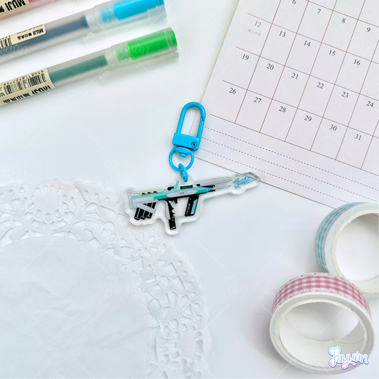 Teal Arc-inspired rifle acrylic charm photographed on a white desk background.