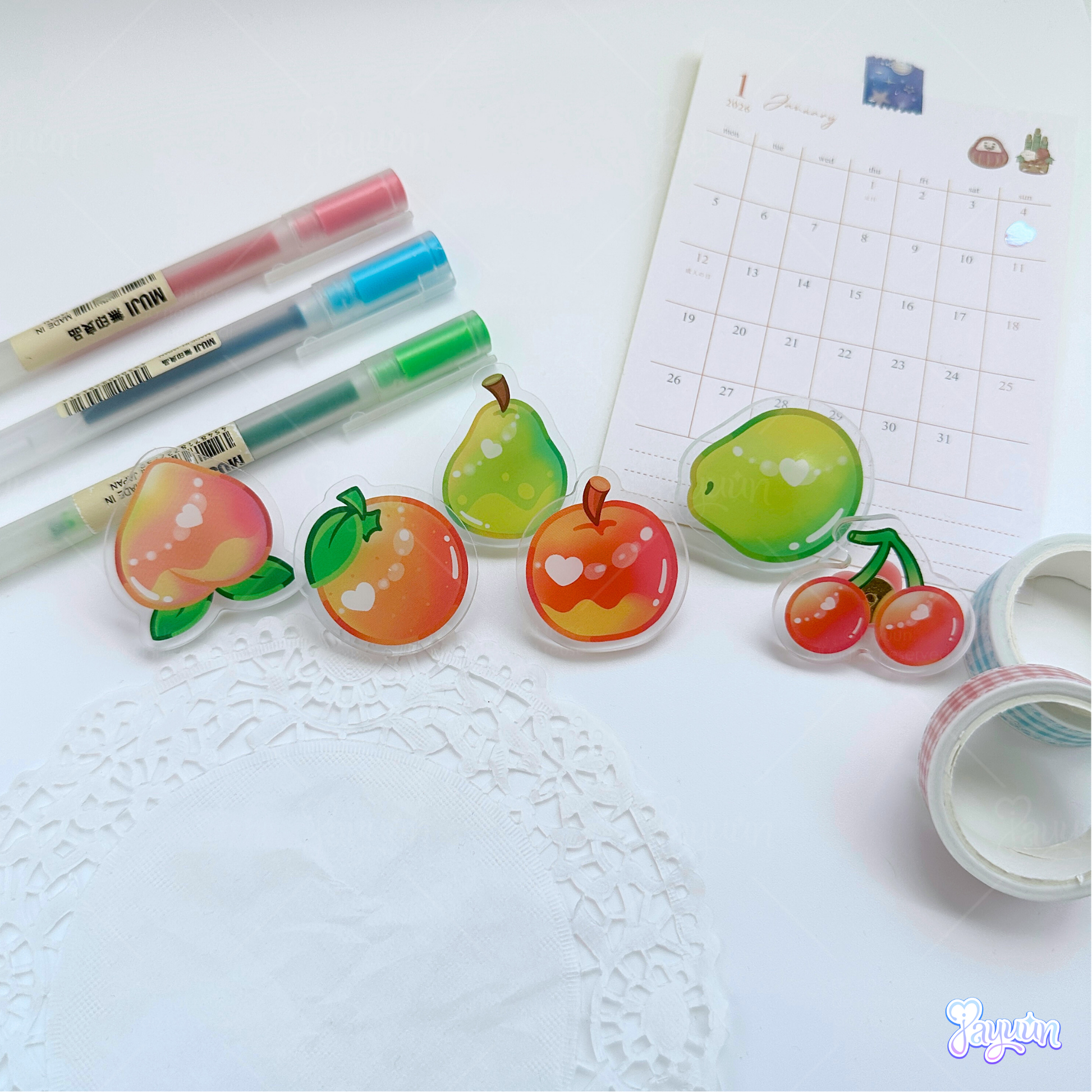 A peach, orange, pear, apple, coconut, and apple acrylic pins photographed on a white desk background.