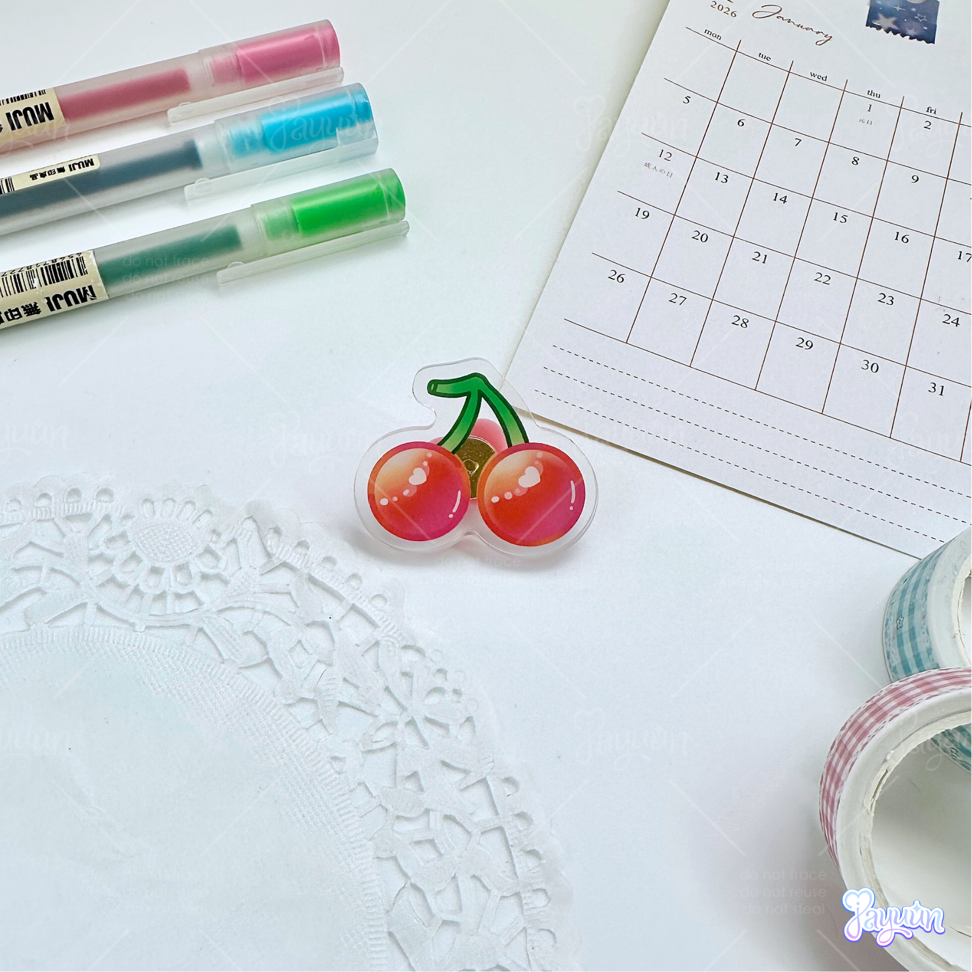 A red cherry acrylic pin photographed on white desk background.