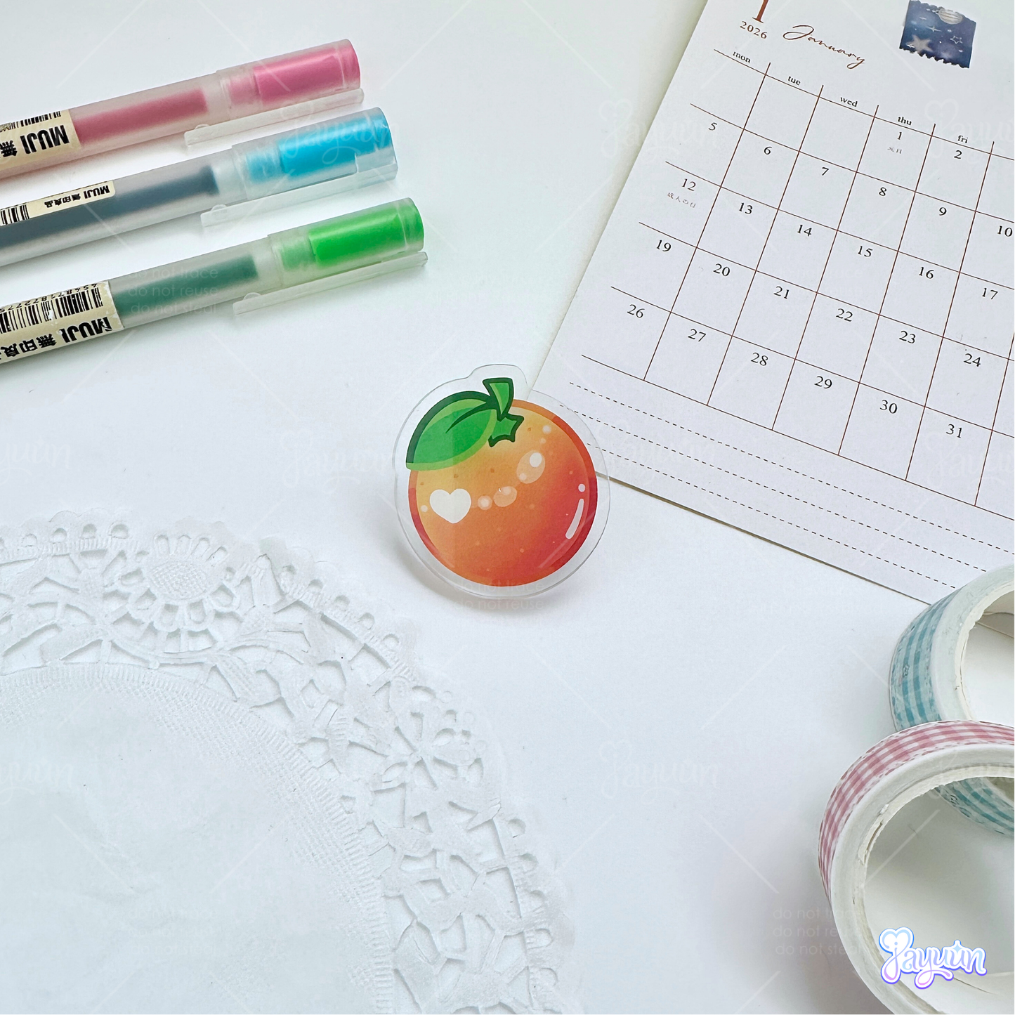 An orange acrylic pin photographed on a white desk background.