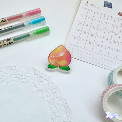A pink peach acrylic pin photographed on a white desk background.