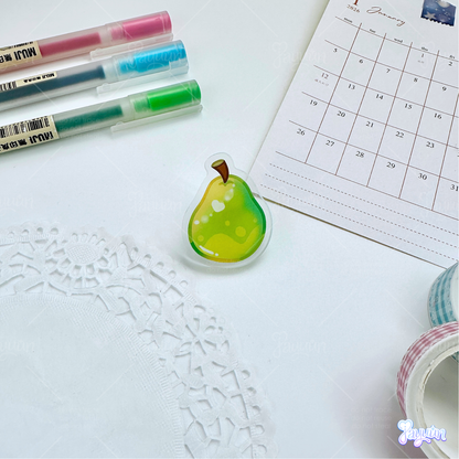 A green pear acrylic pin photographed on a white desk background.