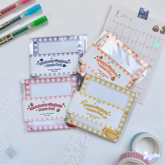 Set of fruit gingham memo pads, consisting of blueberry, orange, strawberry, and lemon, photographed on a white desk background.