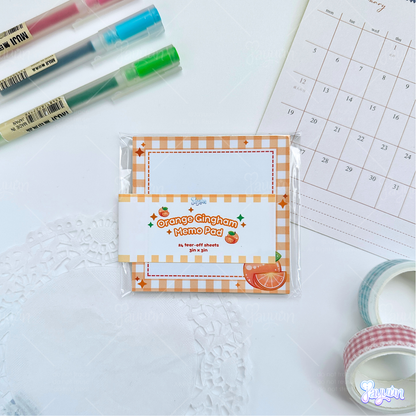 Orange gingham memo pad photographed on a white desk background.