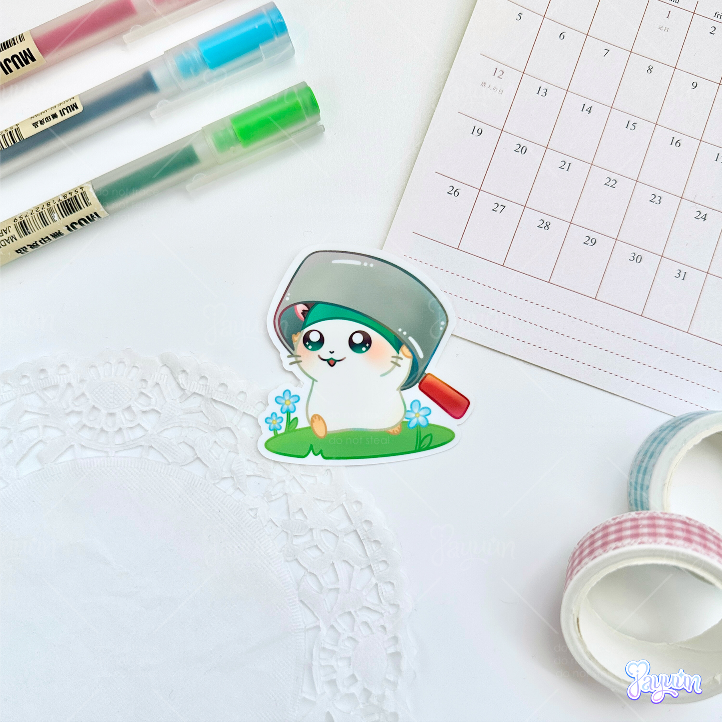 A sticker of Cappy from the cartoon Hamtaro standing on a patch of grass, photographed on a white desk background.