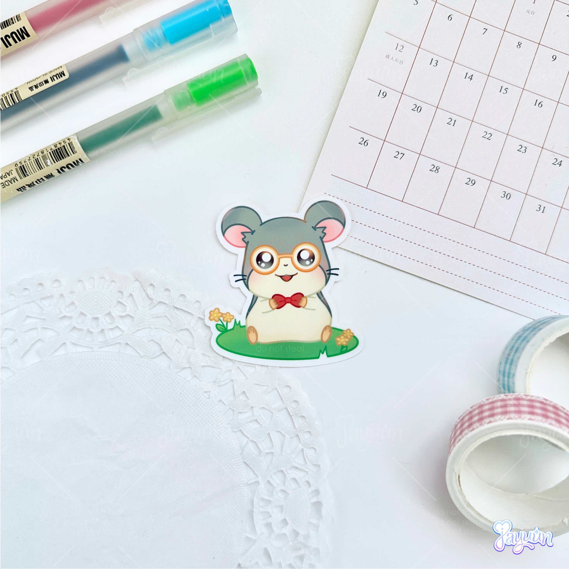 A sticker of Dexter from the cartoon Hamtaro sitting on a patch of grass, photographed on a white desk background.