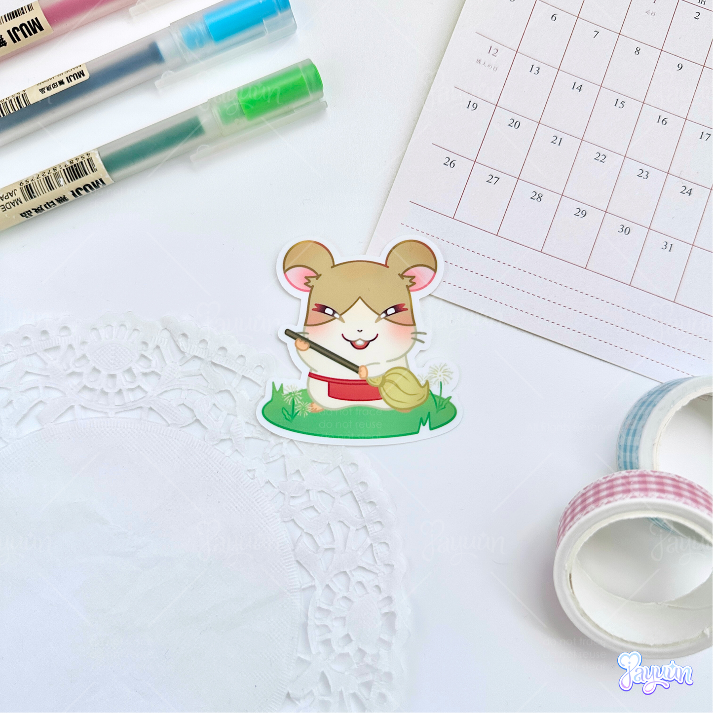 A sticker of Howdy from the cartoon Hamtaro standing on a patch of grass, photographed on a white desk background.