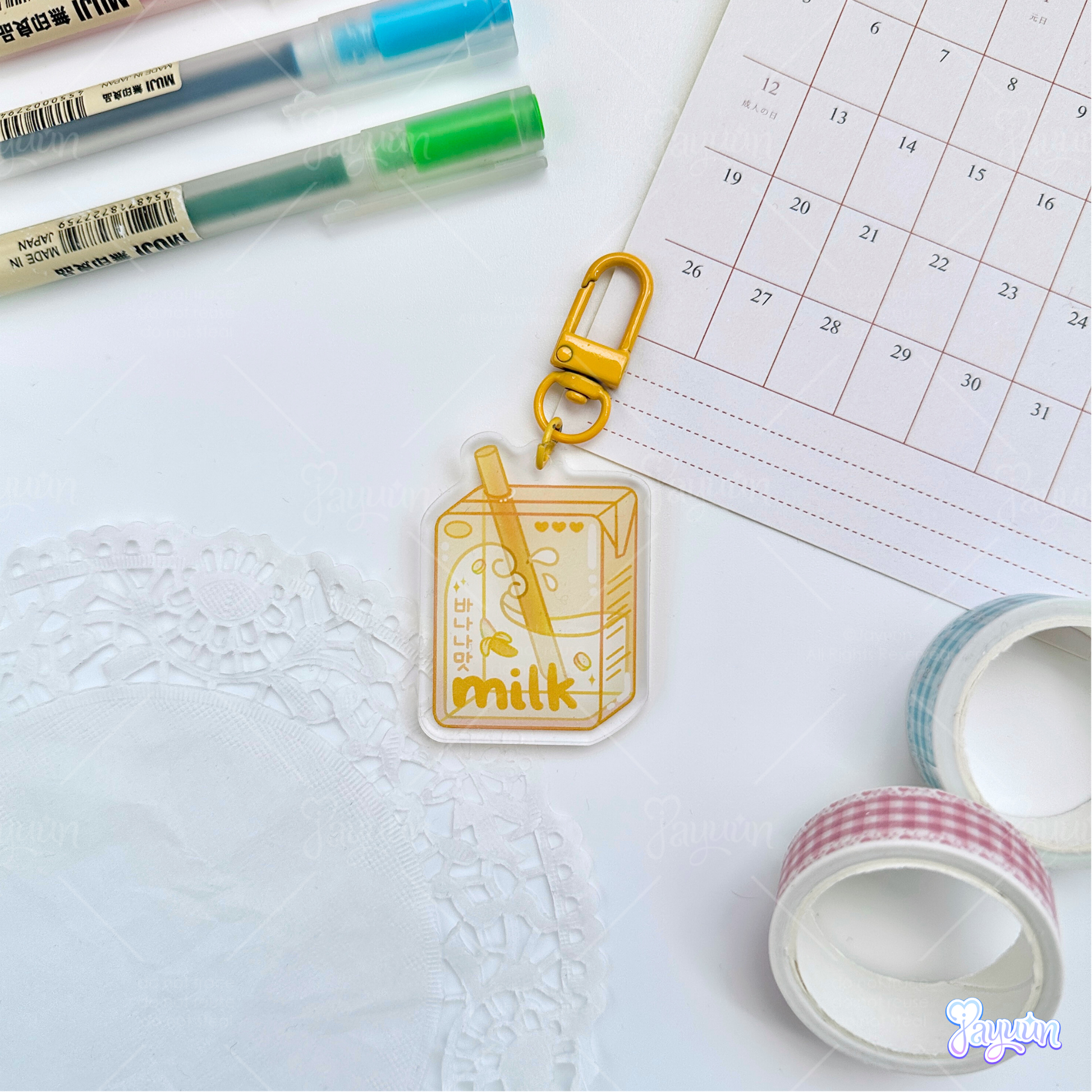 Yellow banana milk carton acrylic keychain photographed on a white desk background.