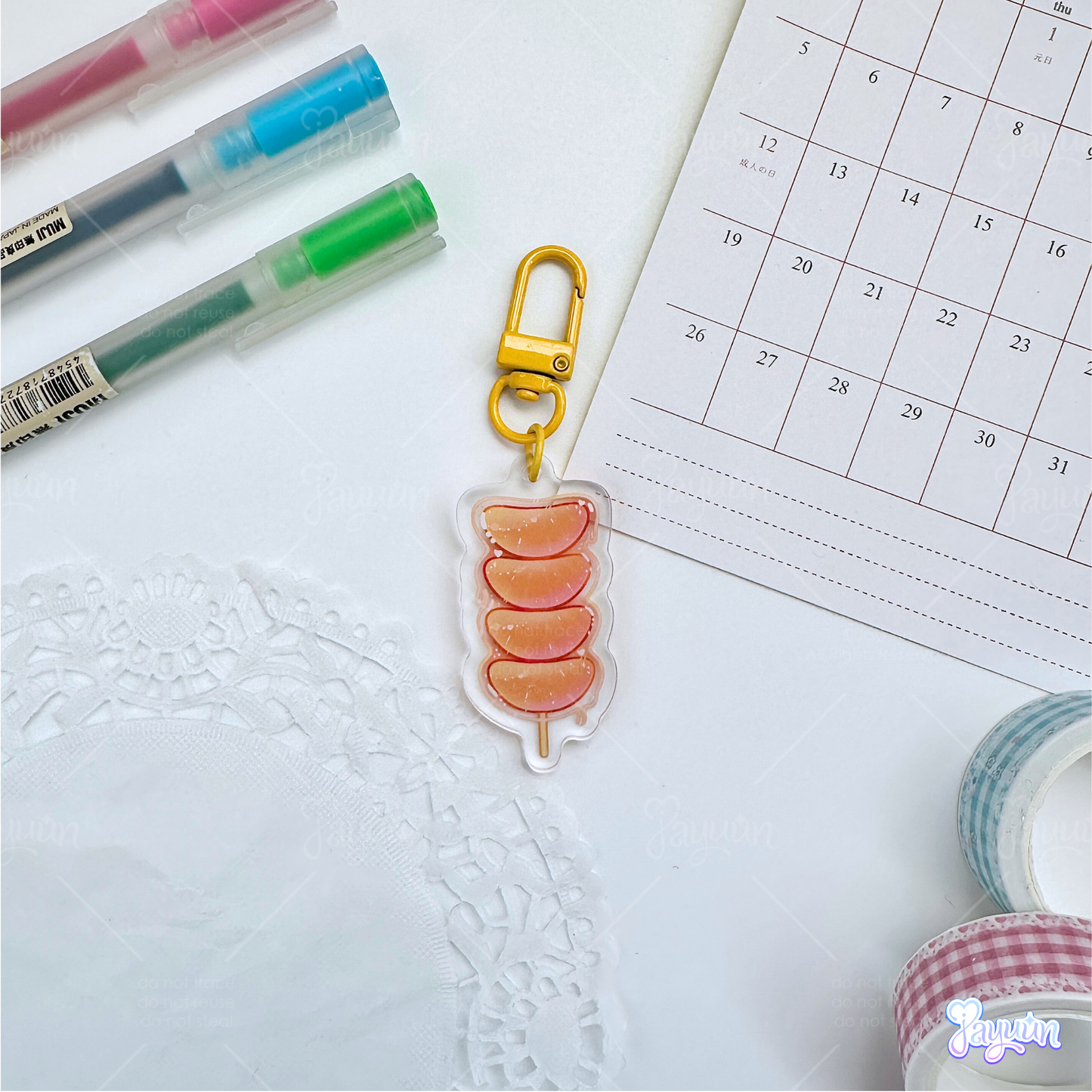 An orange tanghulu acrylic charm photographed on a white desk background.