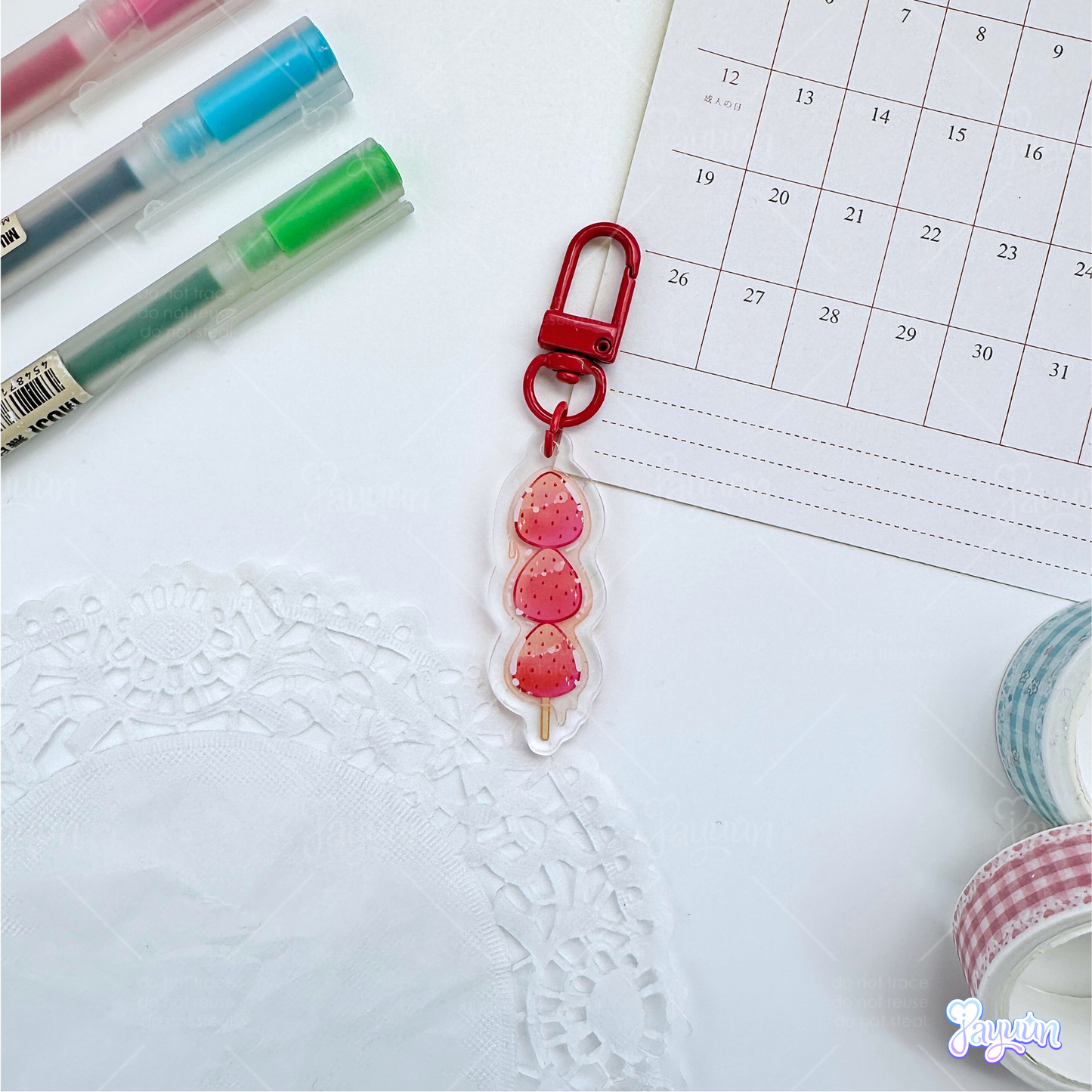 A red strawberry tanghulu acrylic charm photographed on a white desk background.
